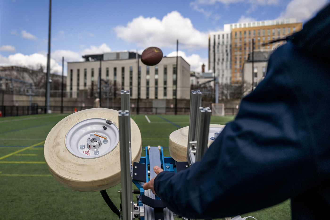 A person launches a football with a machine outside on a turf field.