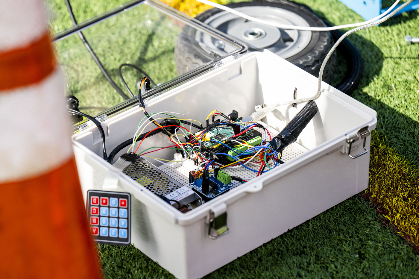 Equipment for an autonomous football-launching machine, including wires, sits in a container outside on the turf. 