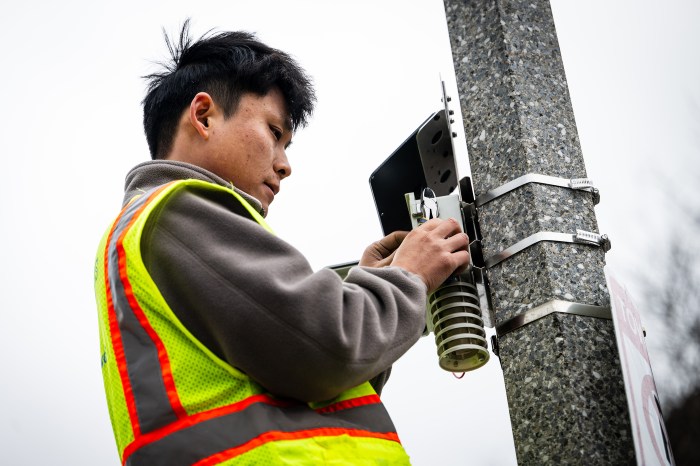 A student checks a heat and noise sensor installed on a light post in Roxbury.