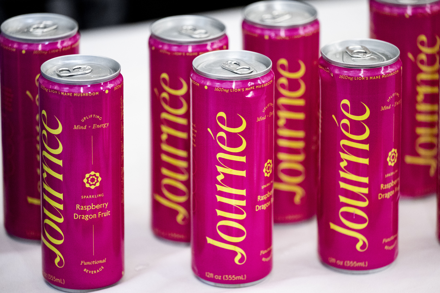Pink, tall, slim cans of 'Journee' energy drink lined up on a white table in Curry Student Center. 