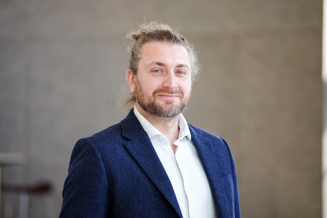 Portrait of someone in a blue suit and white shirt against a concrete background.
