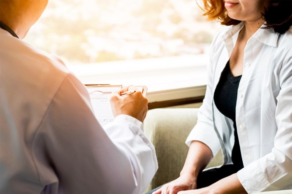A physician in a white lab coat takes a note while a person in a white shirt sits next to them.