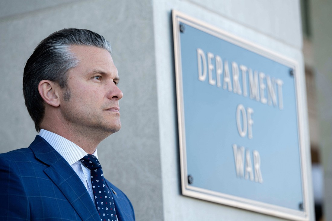 Side profile view of Pete Hegseth standing outside of a building with a plaque on it that says 'Department of War'.