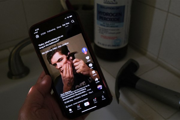A person is holding up a phone depicting a man holding a hammer to his face in a dark bathroom.