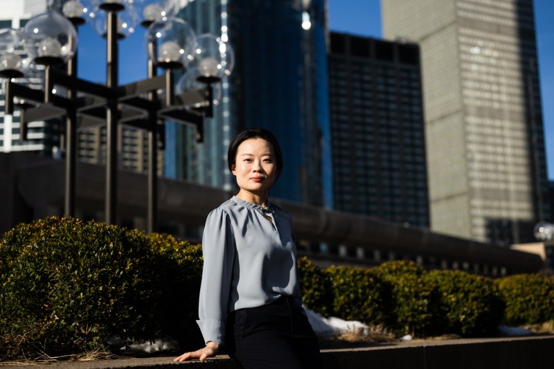 Fang Fang stands in front of a row of bushes with an ornate street lamp behind her and Boston buildings in the background.