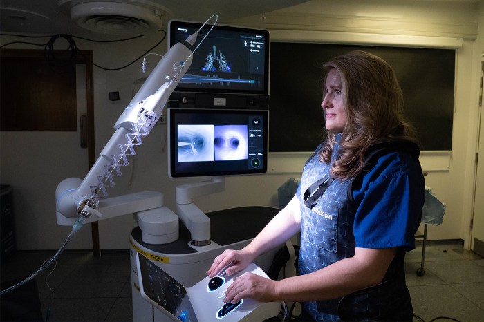 A female doctor, surrounded by screens in a dimly lit room, uses an advanced imaging device with a movable arm.