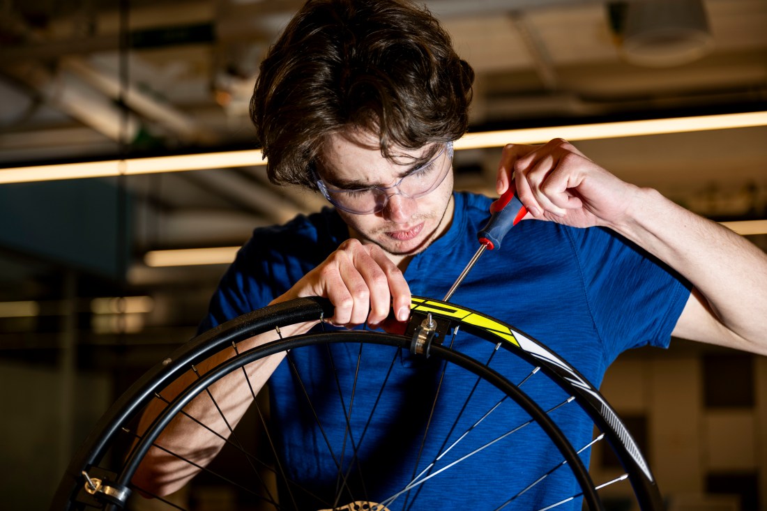 Northeastern student Aydan Kloiber wearing safety glasses while working on fitting a bicycle wheel as part of an affordable wheelchair build. 