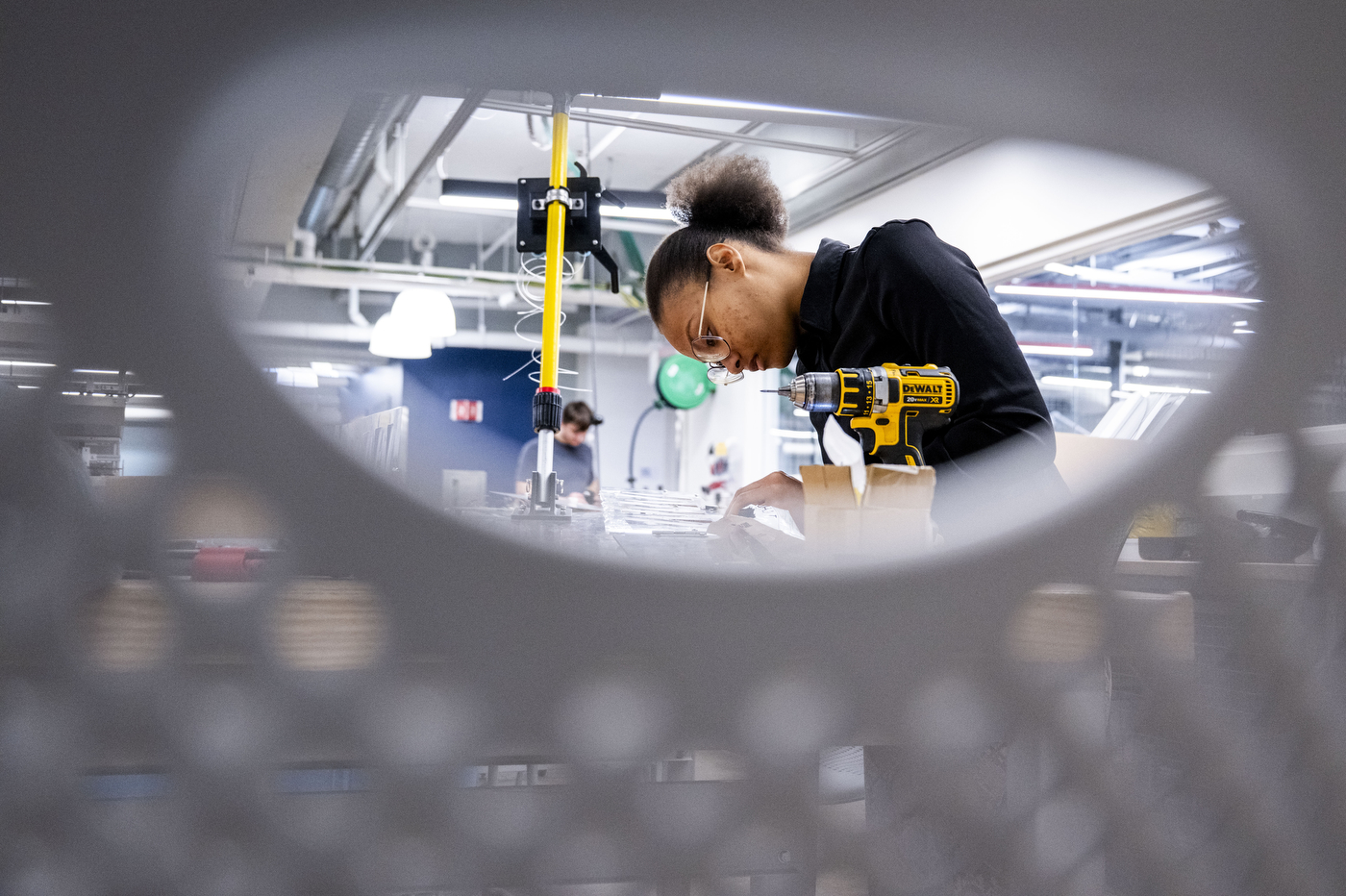 Looking through a piece of equipment, a student working with tools in an engineering lab.