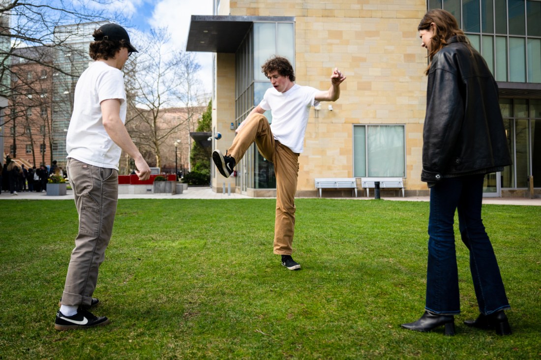 Three students play with a hacky sack in a green space on campus.
