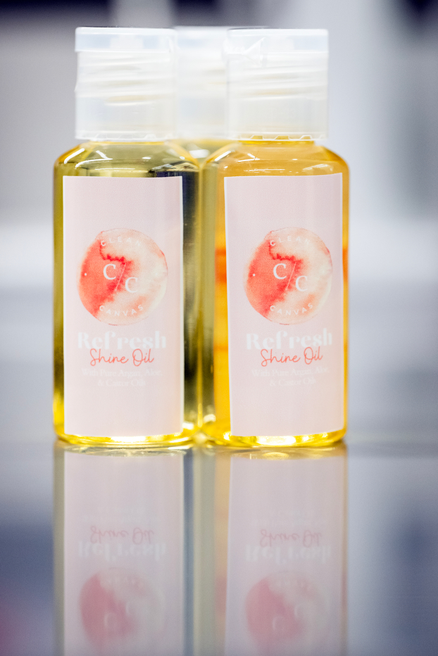 Three small plastic bottles with yellow oil inside. The pink label says Refresh shine oil by Clear Canvas.