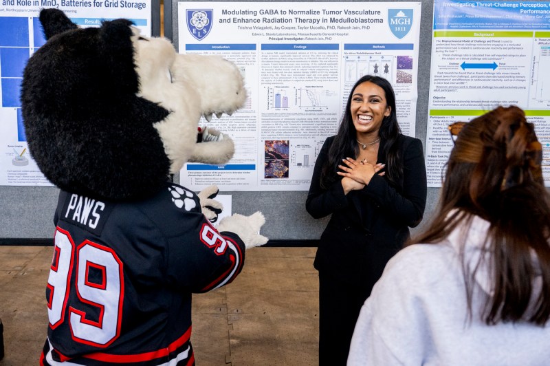 A student smiles as Paws the mascot and another person view her research presentation.