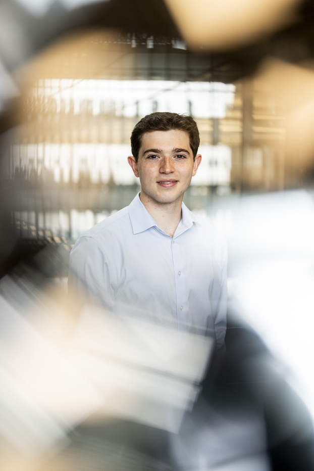 Portrait of Ethan Bengelsforf in a light blue button-down shirt, photographed with a shallow depth of field and warm, blurred bokeh in the background.