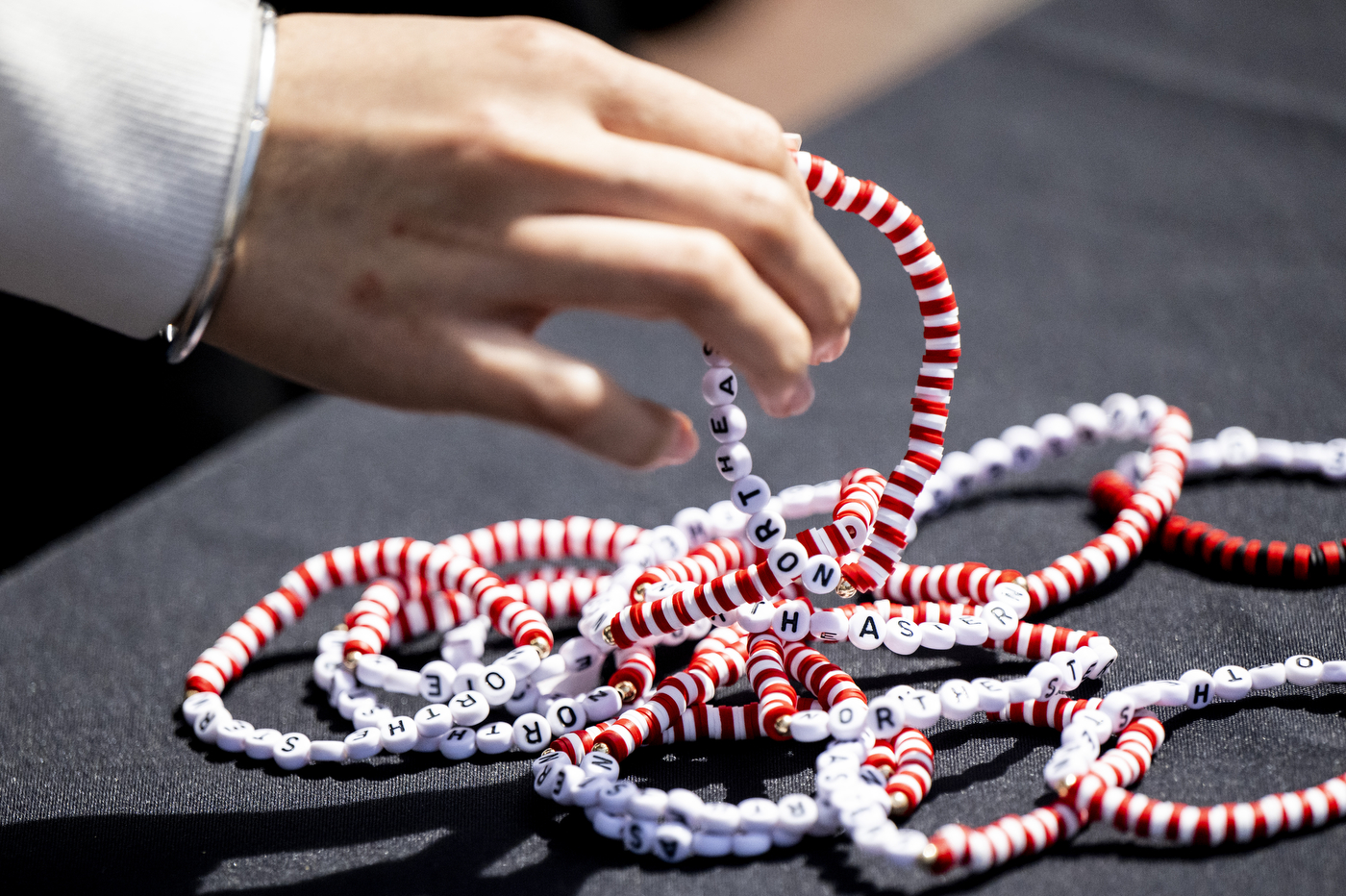 A hand reaches for a pile of red and white beaded bracelets that say 'Northeastern'. 