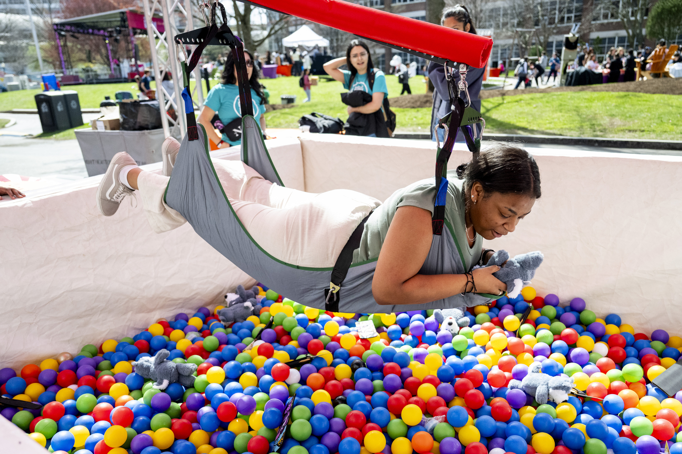 A student hangs over a ball pit of colorful balls in a full body harness. 