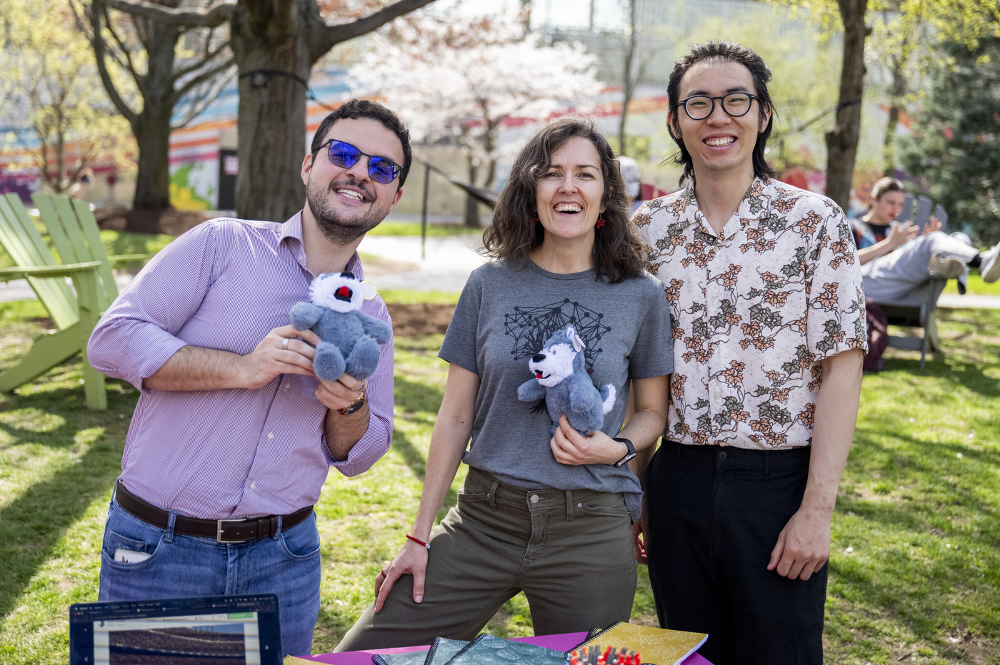 Three people smile while posing with plush huskies. 