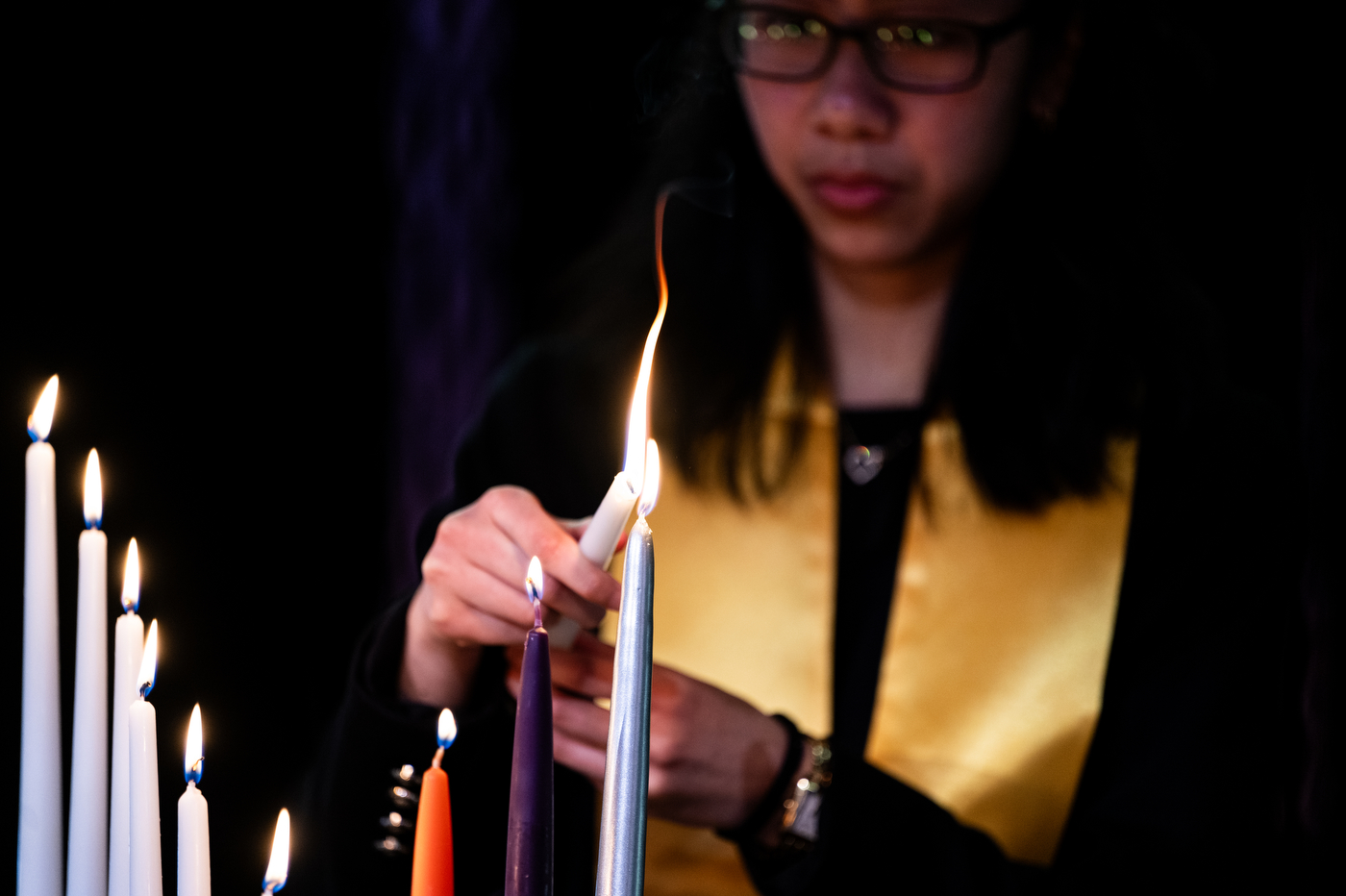 A close up of an inductee carefully lighting a candle.
