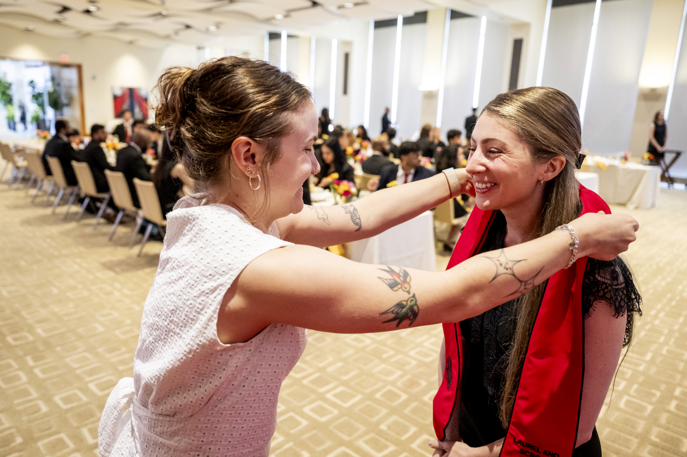 Someone puts a red sash on the shoulders of a recipient at the Laurel and Scroll ceremony