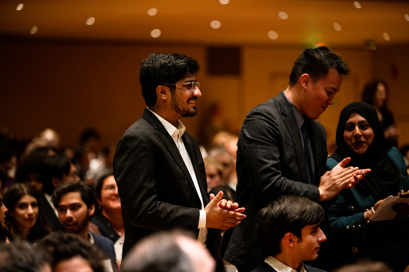 Attendees in the audience applaud during the Academic Honors Convocation ceremony. Three are standing while the rest are seated.
