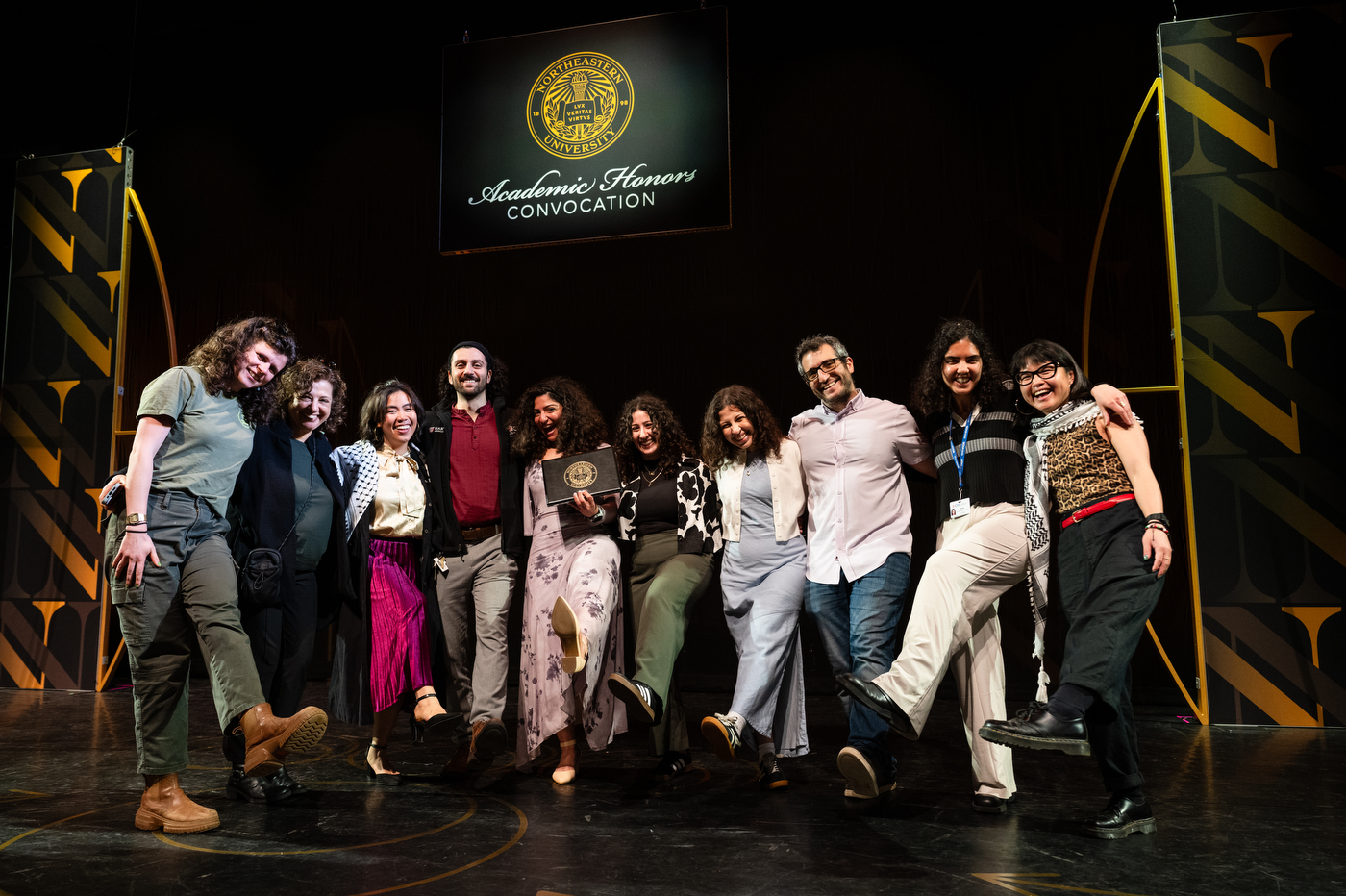 A group of people posing on stage with one leg raised at the Academic Honors Convocation. 