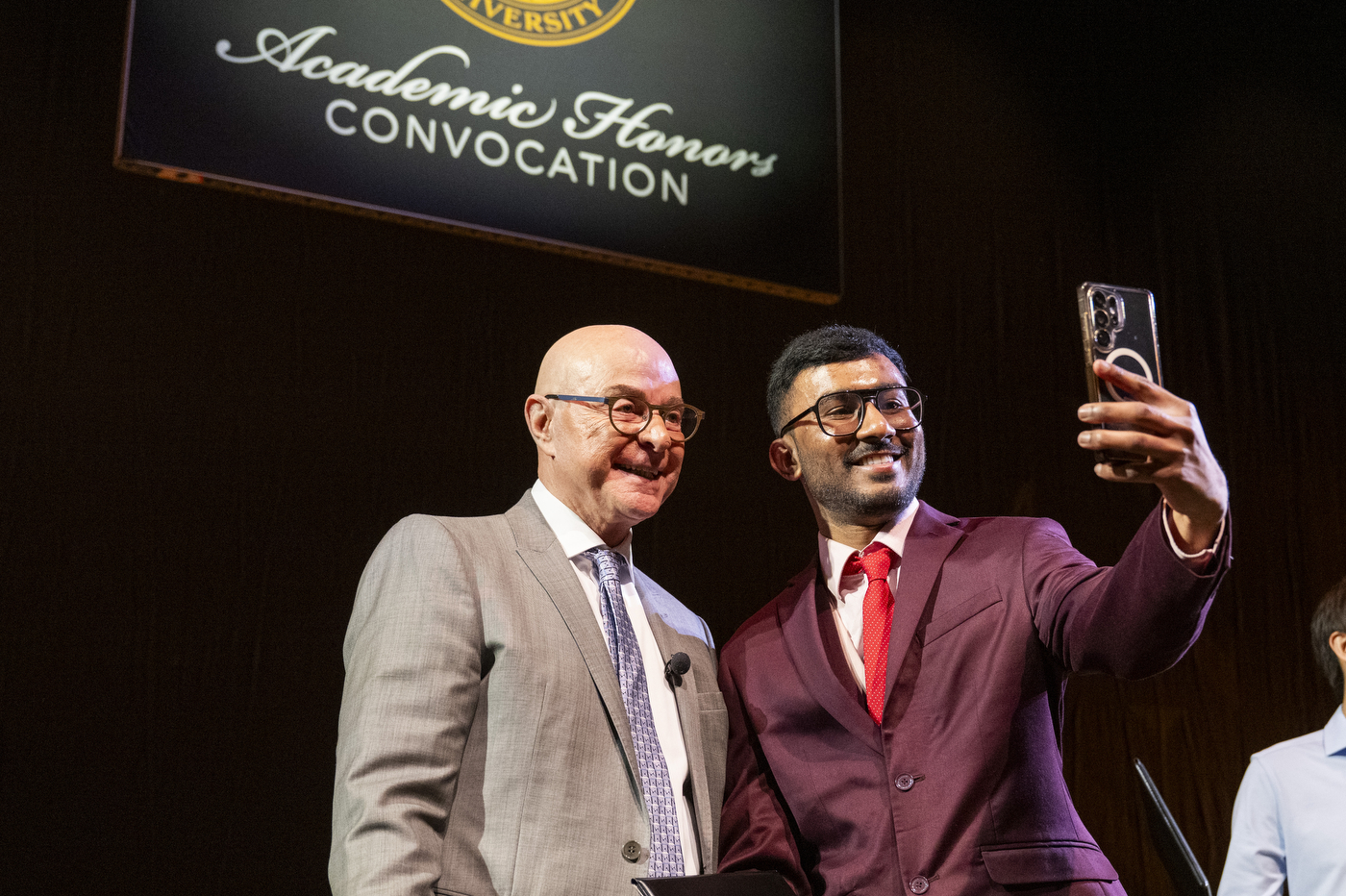 President Aoun poses for a selfie with a student in a maroon suit at the Academic Honors Convocation ceremony.