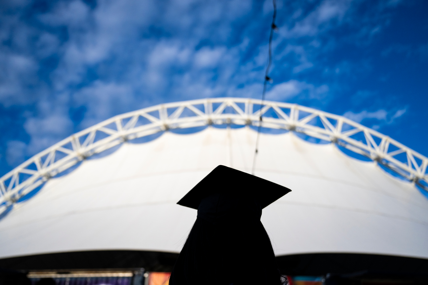 The silhouette of the back of a graduate in front of the Leader Bank Pavilion in the background.