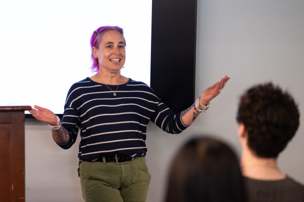 Laney Strange, a Northeastern University computer science professor with purple hair, speaks with her arms raised at the Last Lecture 2026, with students visible in the foreground.
