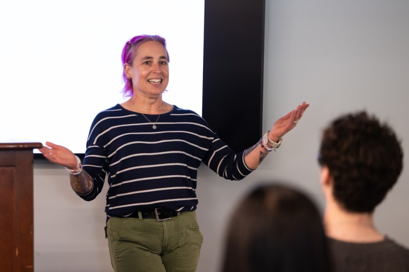 Laney Strange, a Northeastern University computer science professor with purple hair, speaks with her arms raised at the Last Lecture 2026, with students visible in the foreground.