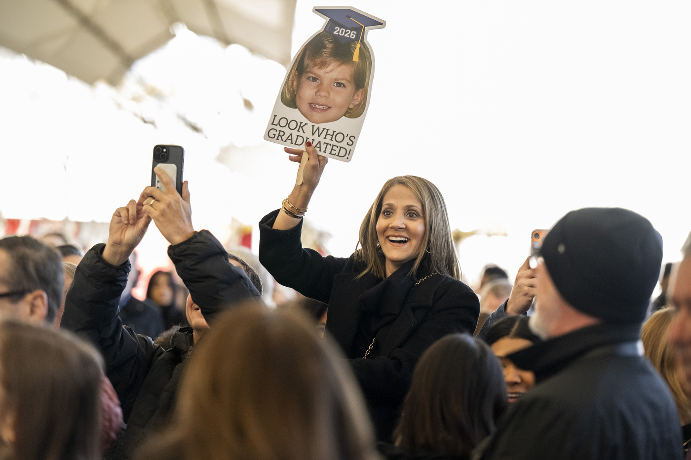The family of a graduate holds up a sign with a face on it that says "look who's graduated?"