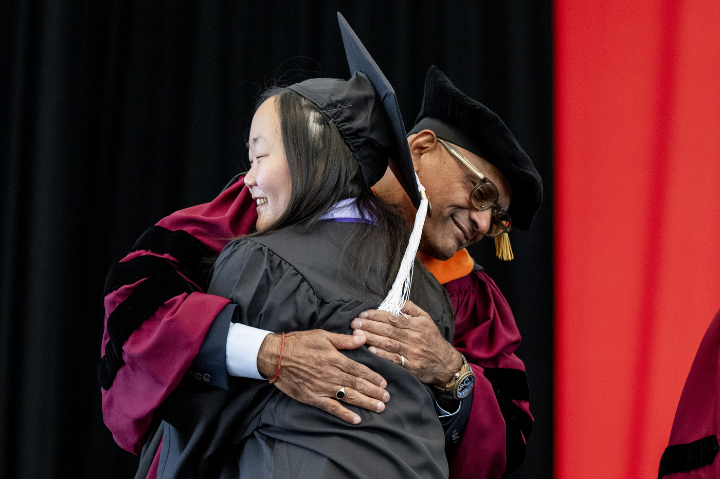 A graduate embraces a faculty member on stage.
