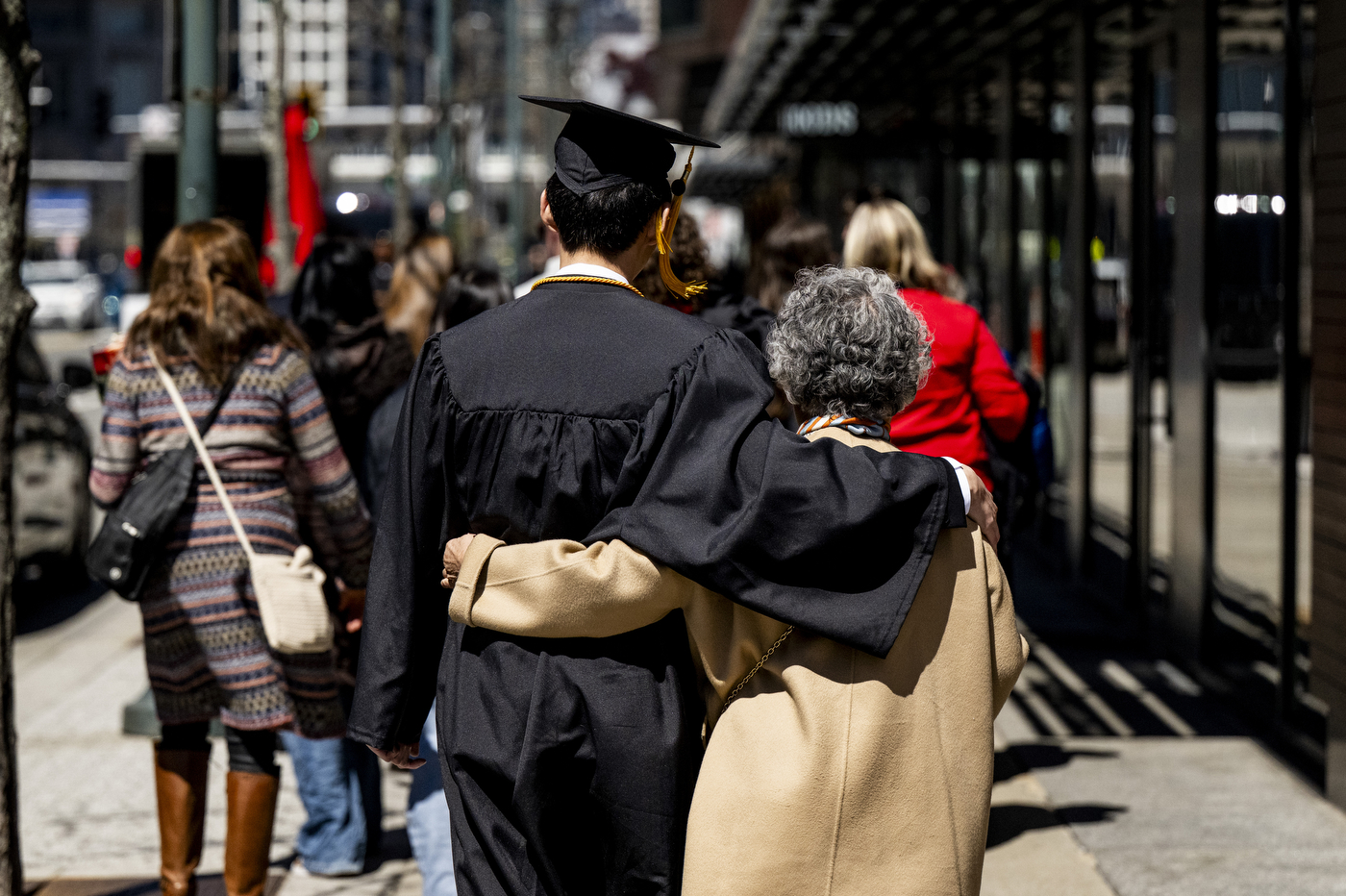 A graduate walks away from the camera with his arm around a family member.