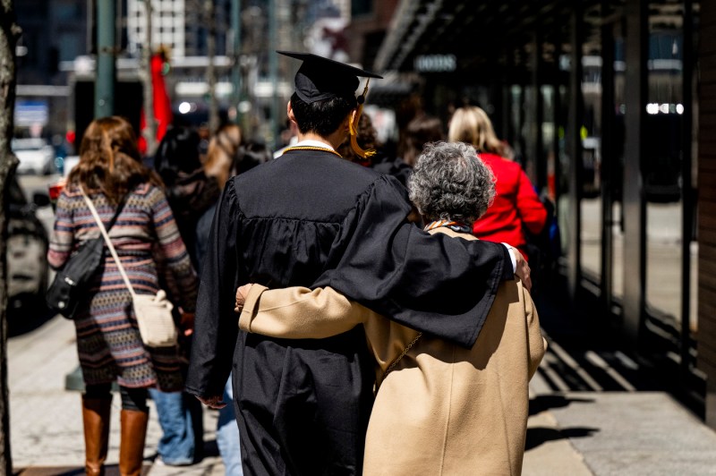 A shot of a graduate and family member walking away from teh camera with their arms around each other.