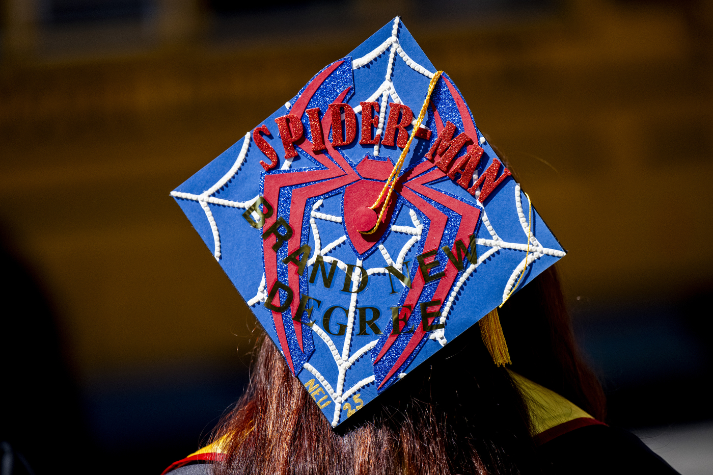 A close up of a decorate grad cap that is blue, red and glittery with a Spiderman logo.