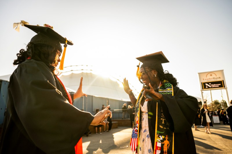 Two graduate caught mid-dance with the sun shining in the background.