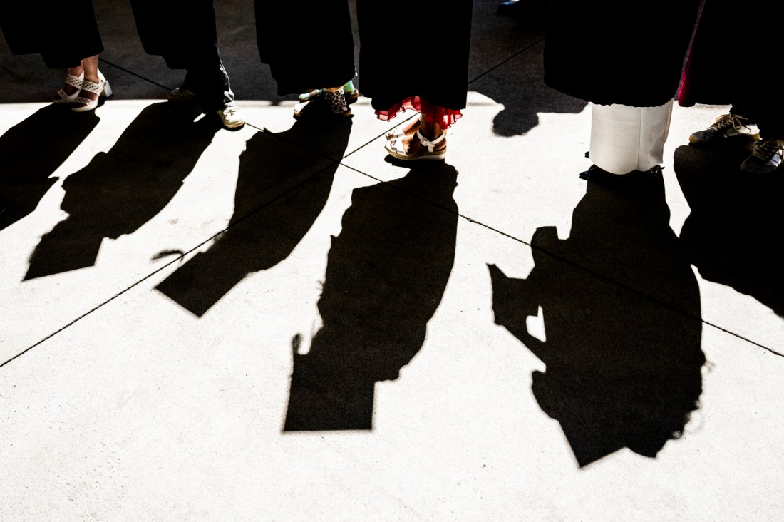 A close up of the shadows of graduates on the ground, showing the silhouettes of their caps and gowns.