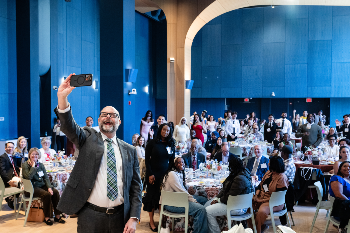 Ken Henderson taking a selfie on an iPhone at the front of a crowded Curry Ballroom.