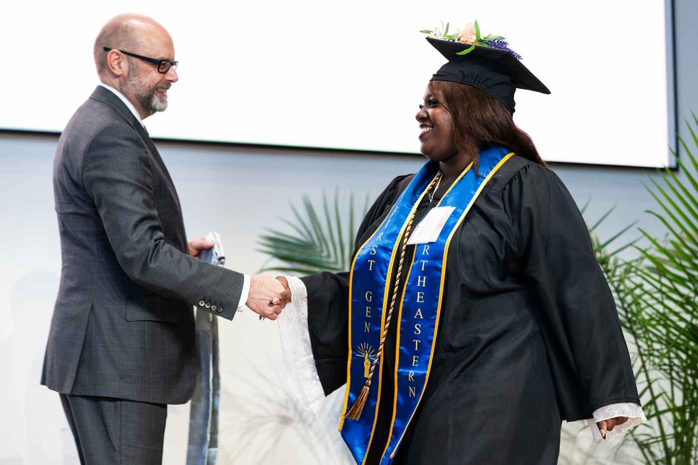 Ken Henderson and a graduate shaking hands as the graduate walks across the stage.