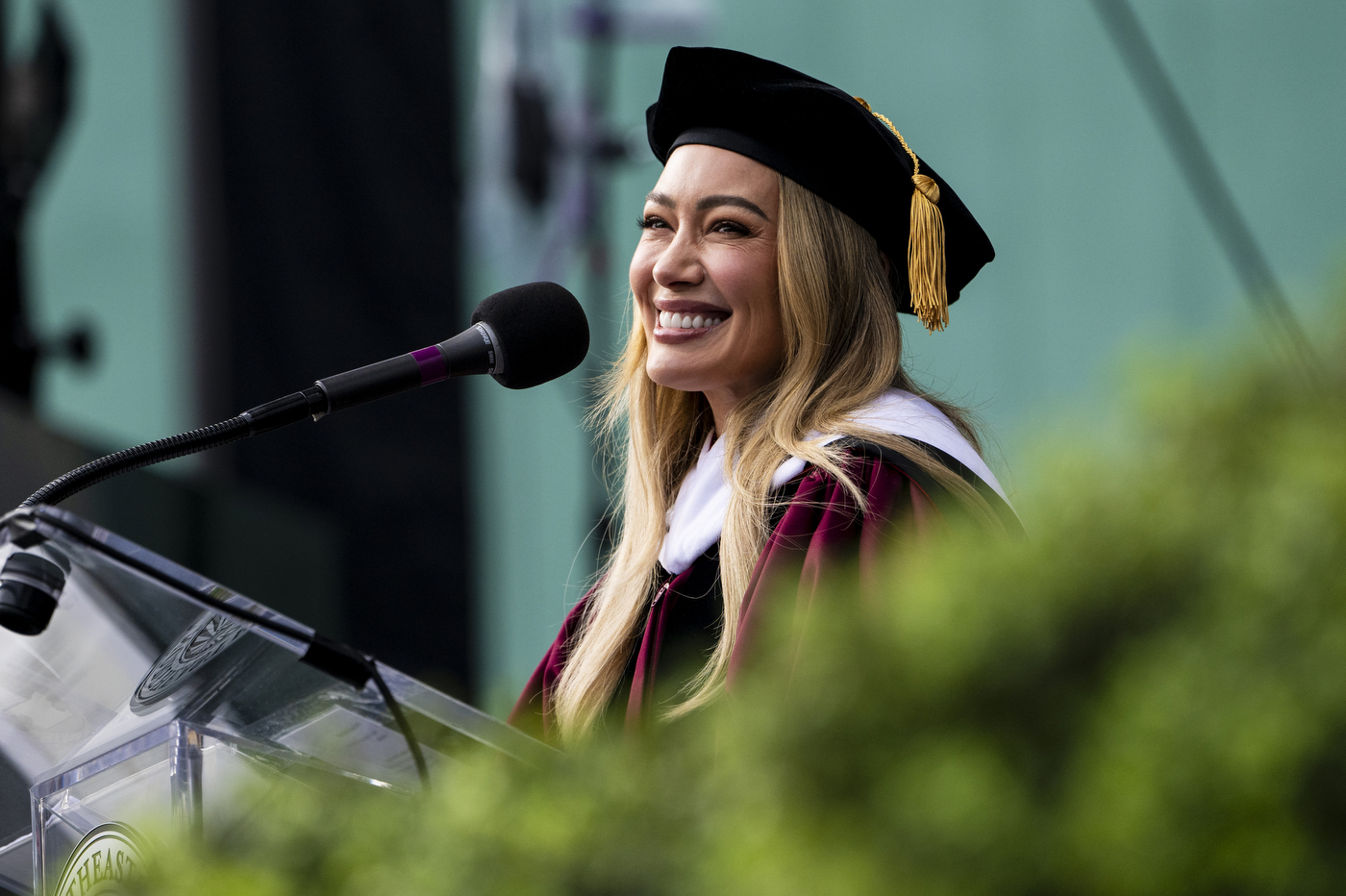 Speaker Hilary Duff smiles while wearing regalia at the podium.