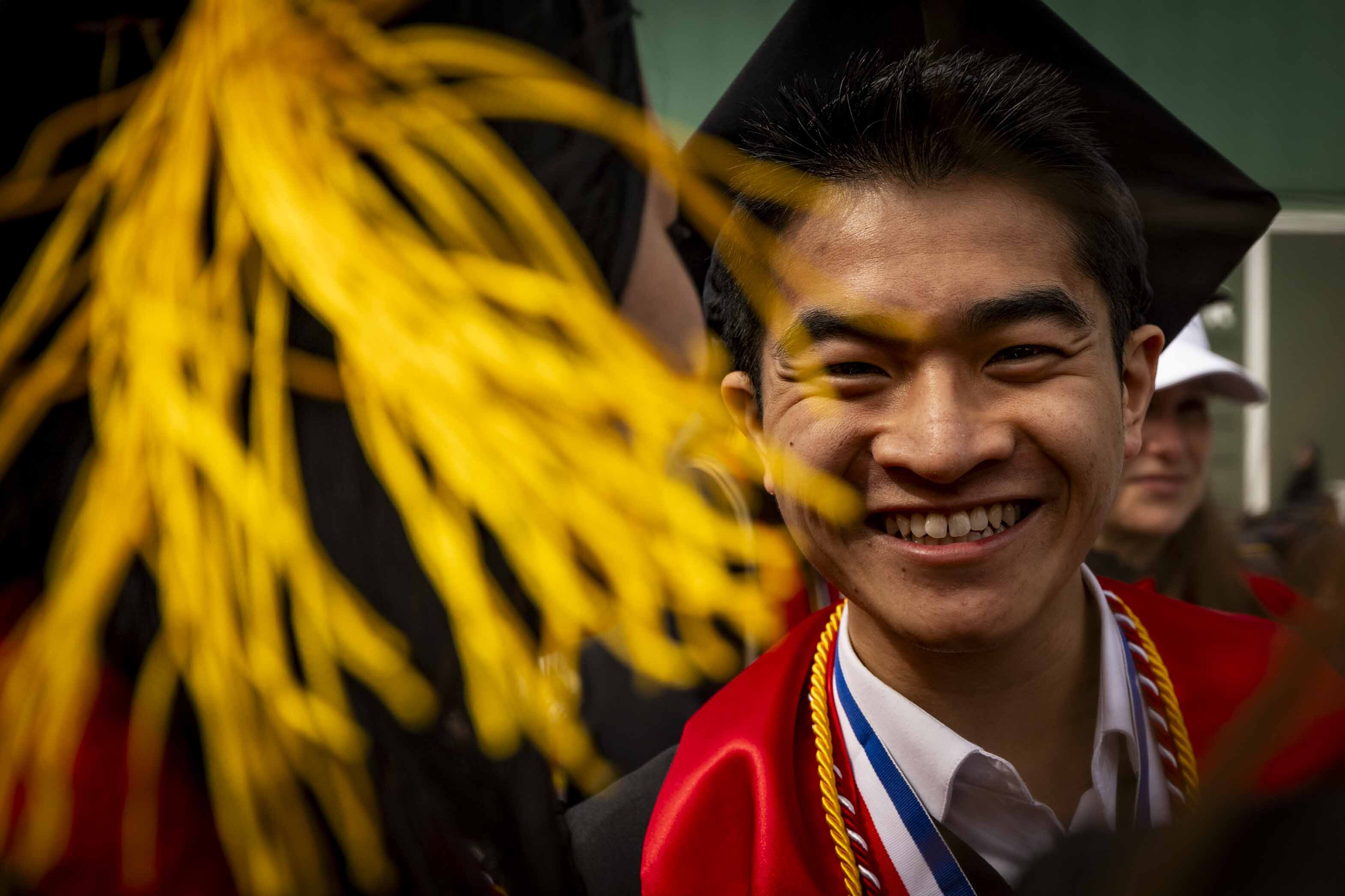 A smiling Northeastern University  wearing a cap, gown, and honor cords at the commencement ceremony.