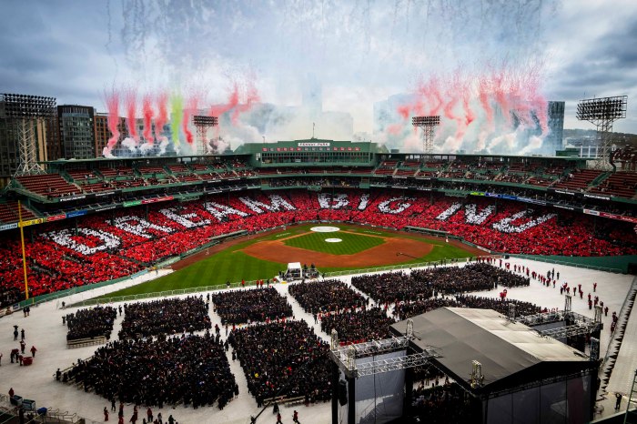 Fireworks and colored smoke soar into the air above Fenway Park at Commencement 2026. The stands are white and red, spelling out Dream Big NU