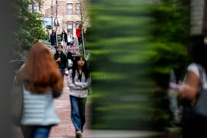 Students walk through campus buildings, with a camera blur effect.