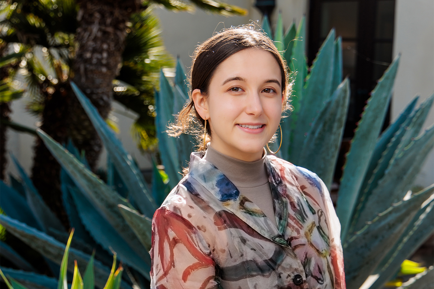 Northeastern University graduate Lauren Conrow smiles in front of large tropical plants, wearing a colorful floral jacket.