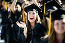 A person wearing a cap and gown cheers and claps excitedly at the 2025 undergraduate Commencement ceremony at Fenway park.
