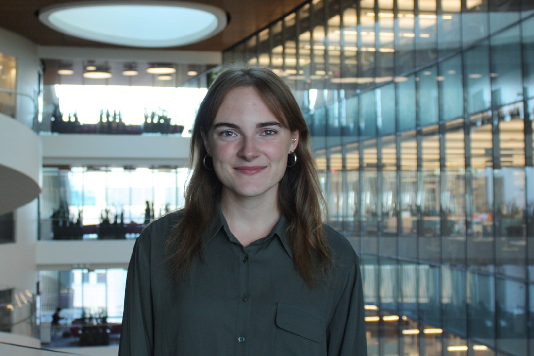 Brooke Rhodes stands in a modern glass atrium, smiling at the camera.