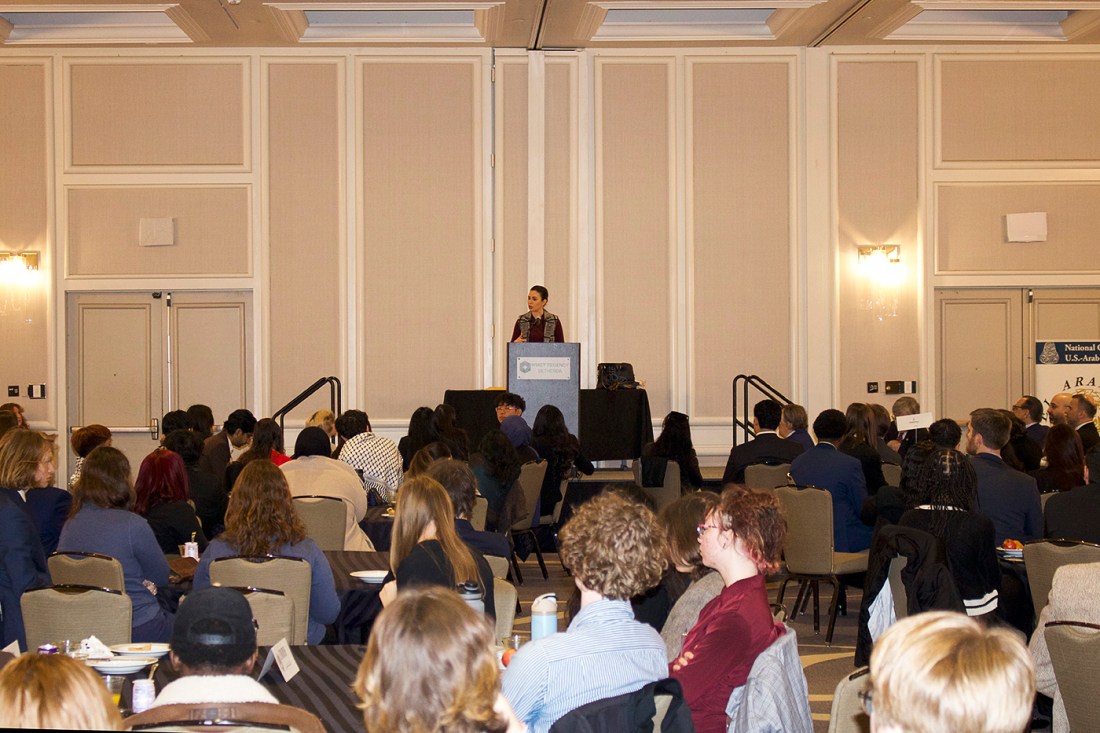 Speaker addresses a large audience of students seated in a conference hall.