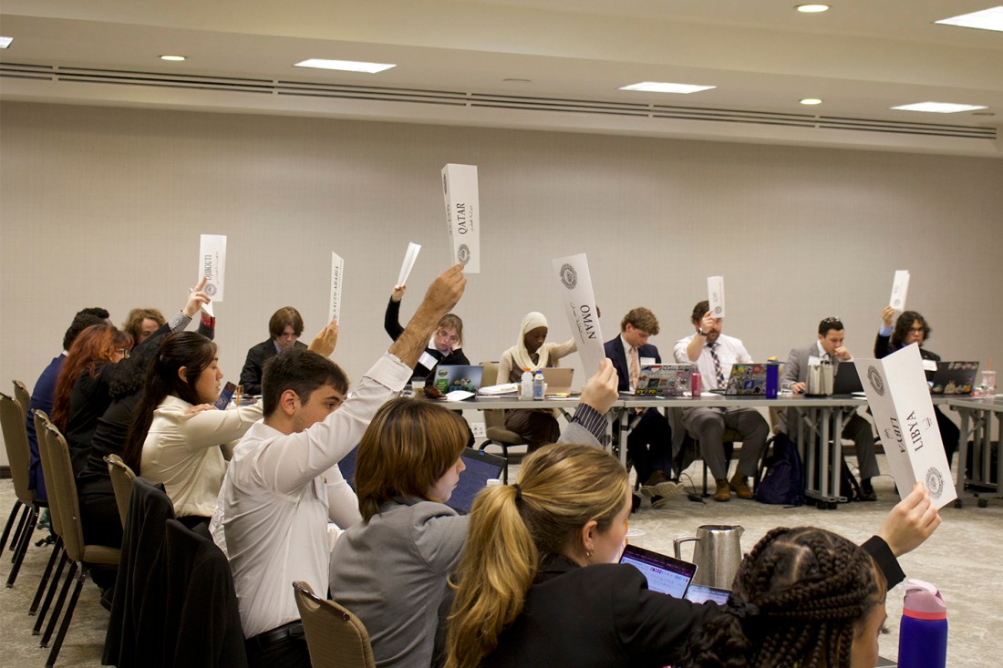Students seated around a conference table raise placards to vote during a committee session.