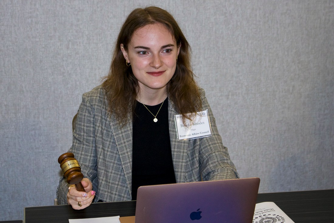 Student chair holding a gavel sits behind a laptop, overseeing a formal debate session.