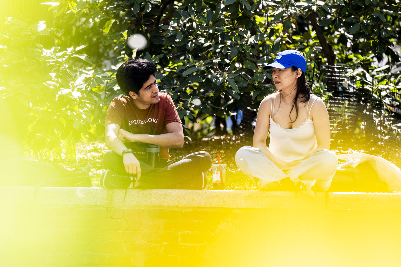 Two students sit on a brick wall in mid-conversation.