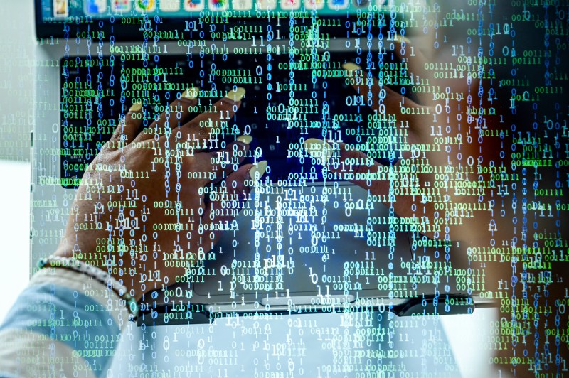 A closeup of hands typing on a laptop with a colorful overlay of  ones and zeroes.