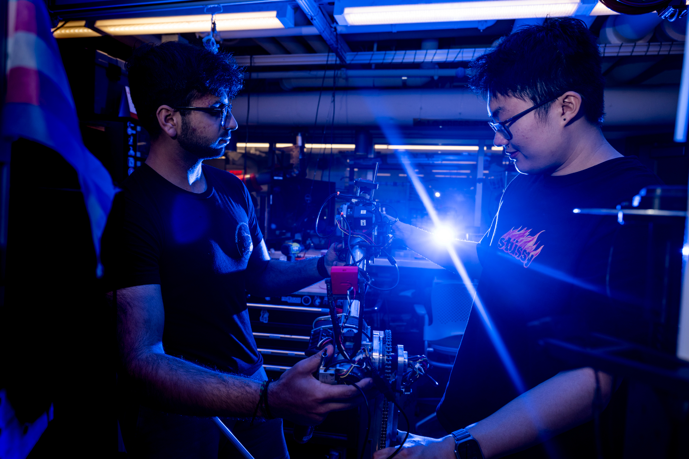 Shaan Merchant and Anthony Wang work in a robotics lab surrounded by blue light in preparation for the University Rover Challenge.