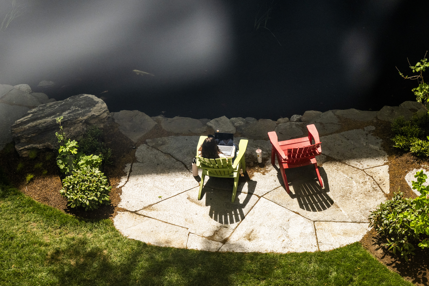 A top down view of a person sitting in a lawn chair by the koi pond.